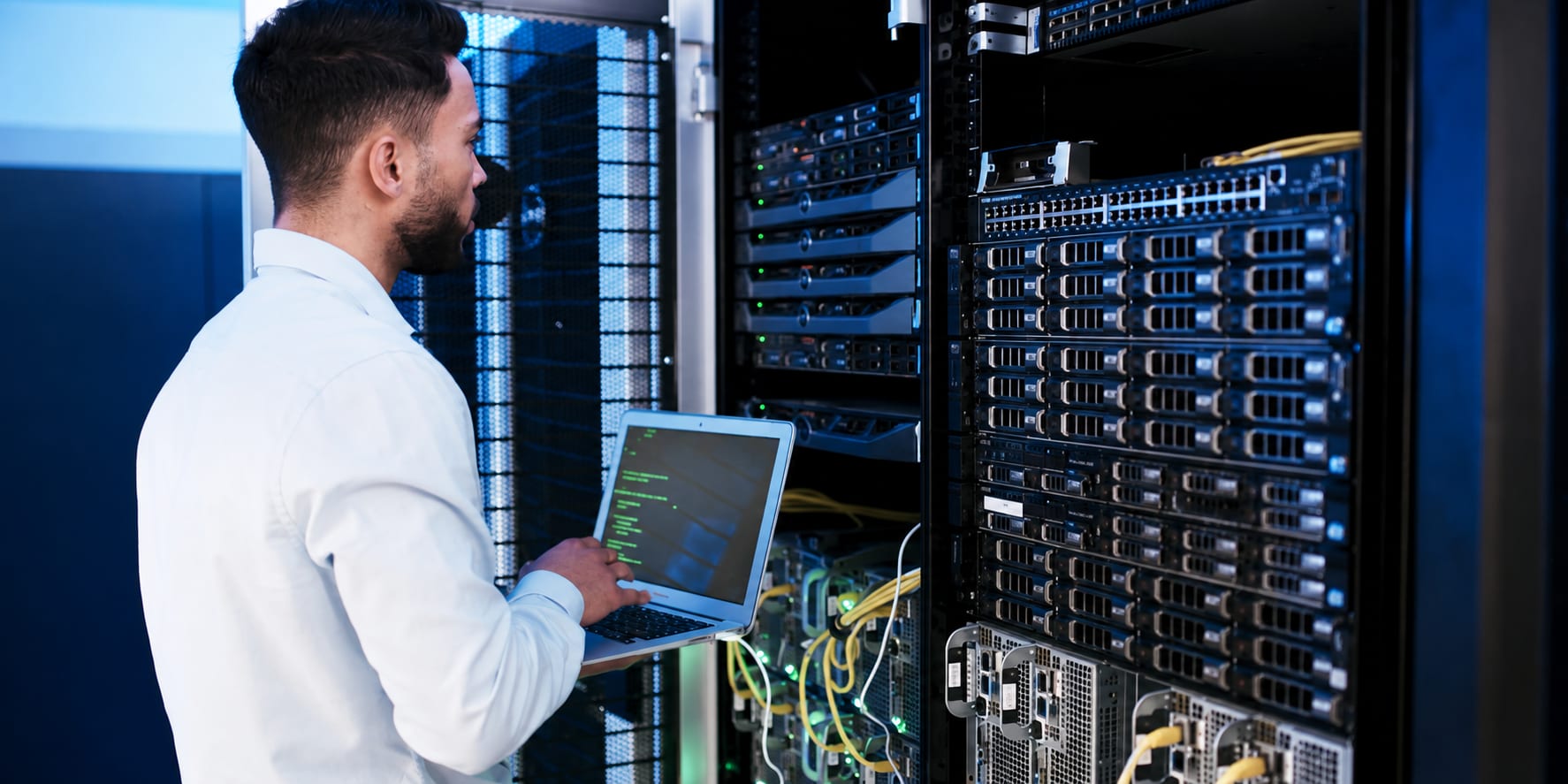 A technician using a laptop beside server racks in a data centre