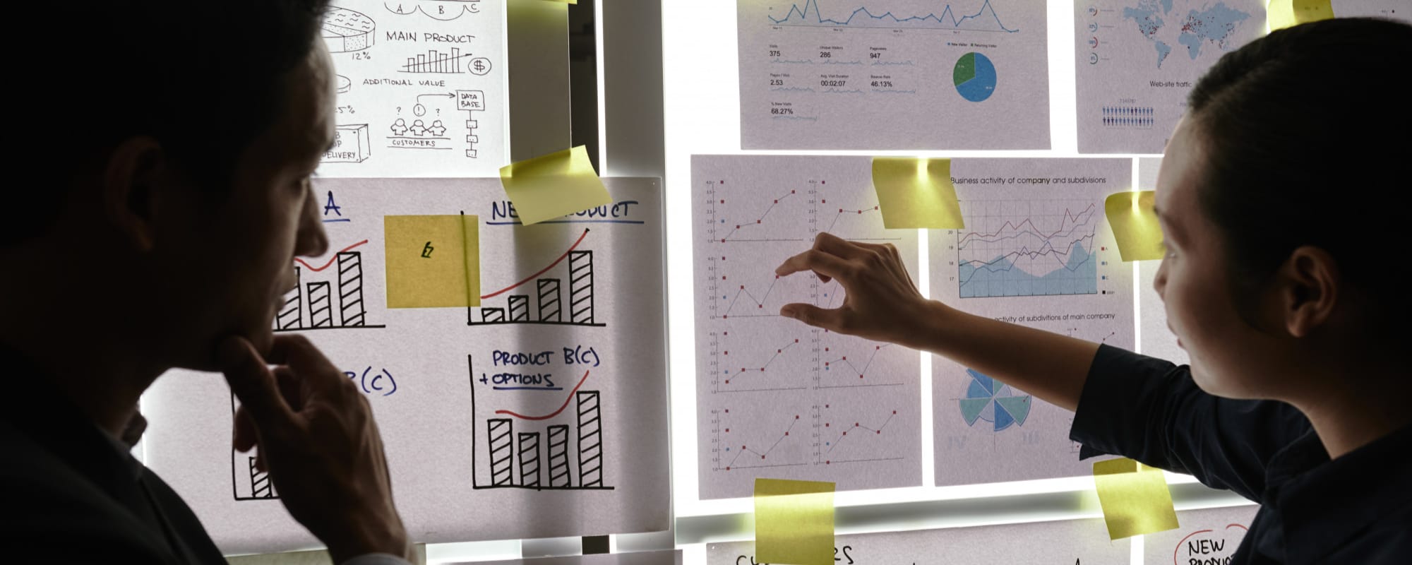 Two colleagues working through charts pinned across a lit wall