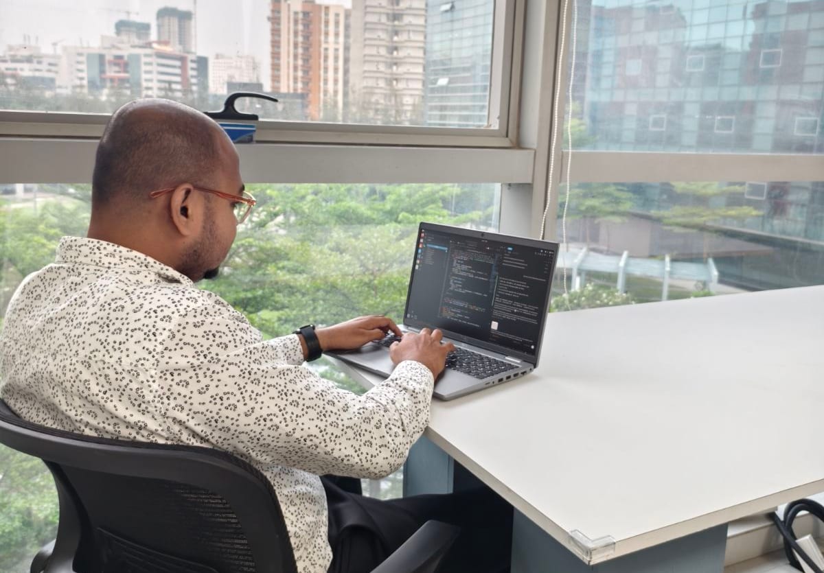 An engineer working at a laptop beside the office windows
