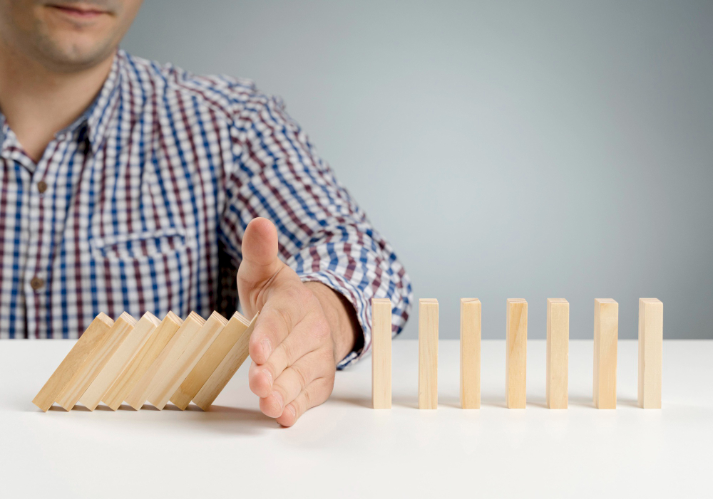 A hand stopping a row of falling dominoes before they reach the standing ones