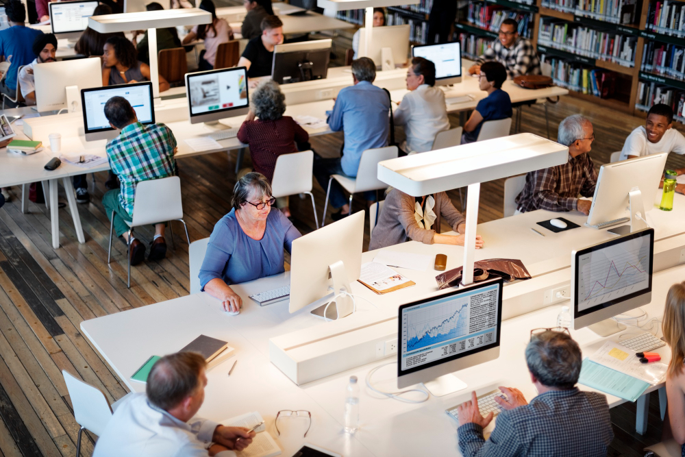 An overhead view of many people working at rows of desktop workstations
