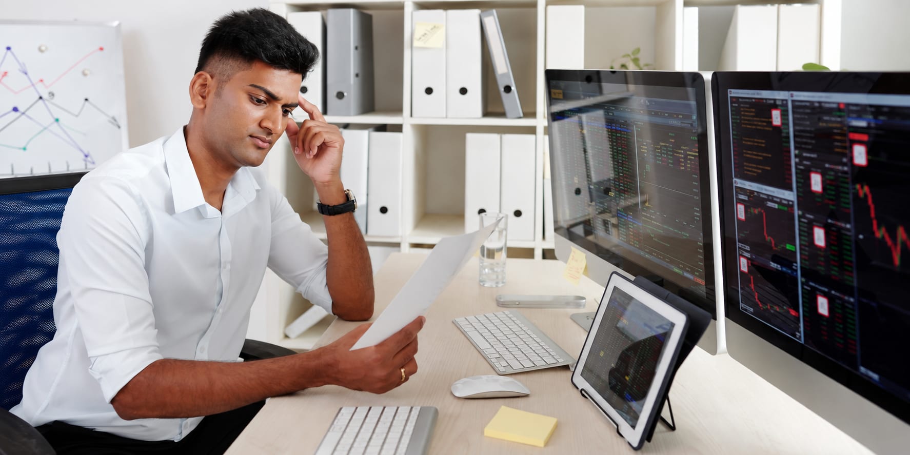 A software engineer reviewing a document beside multiple monitors