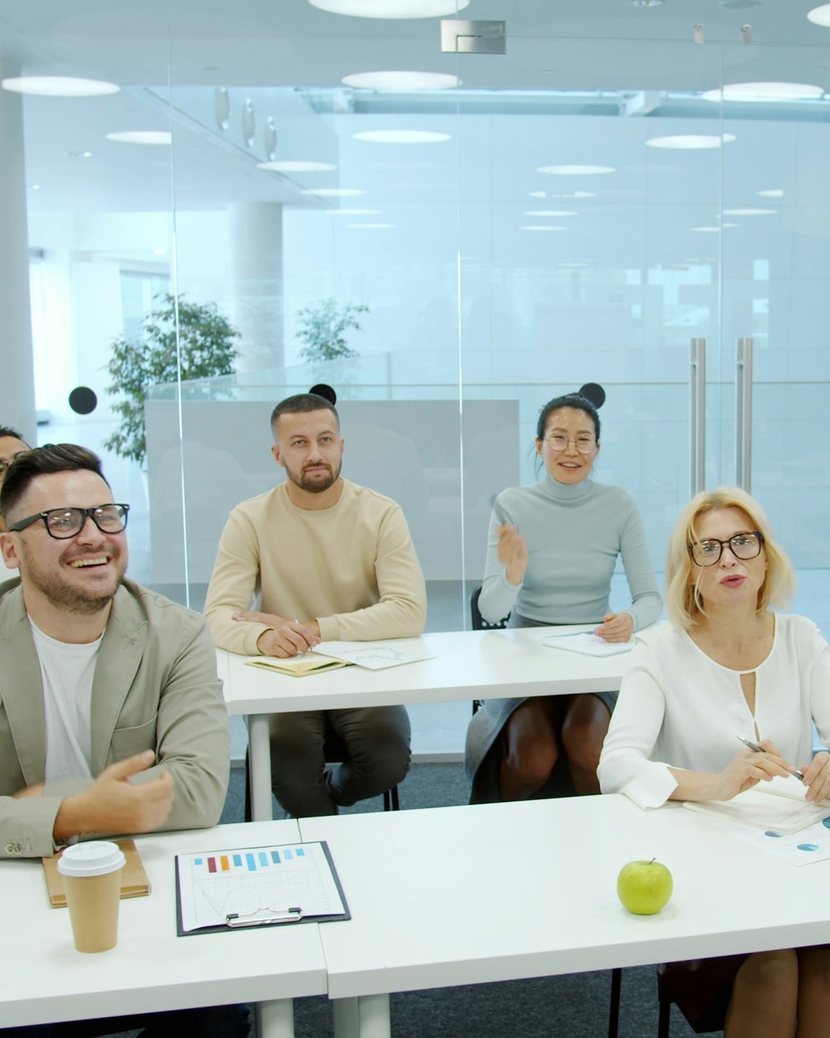 Four people seated at tables in a training room, working through a course with a presentation screen at the front