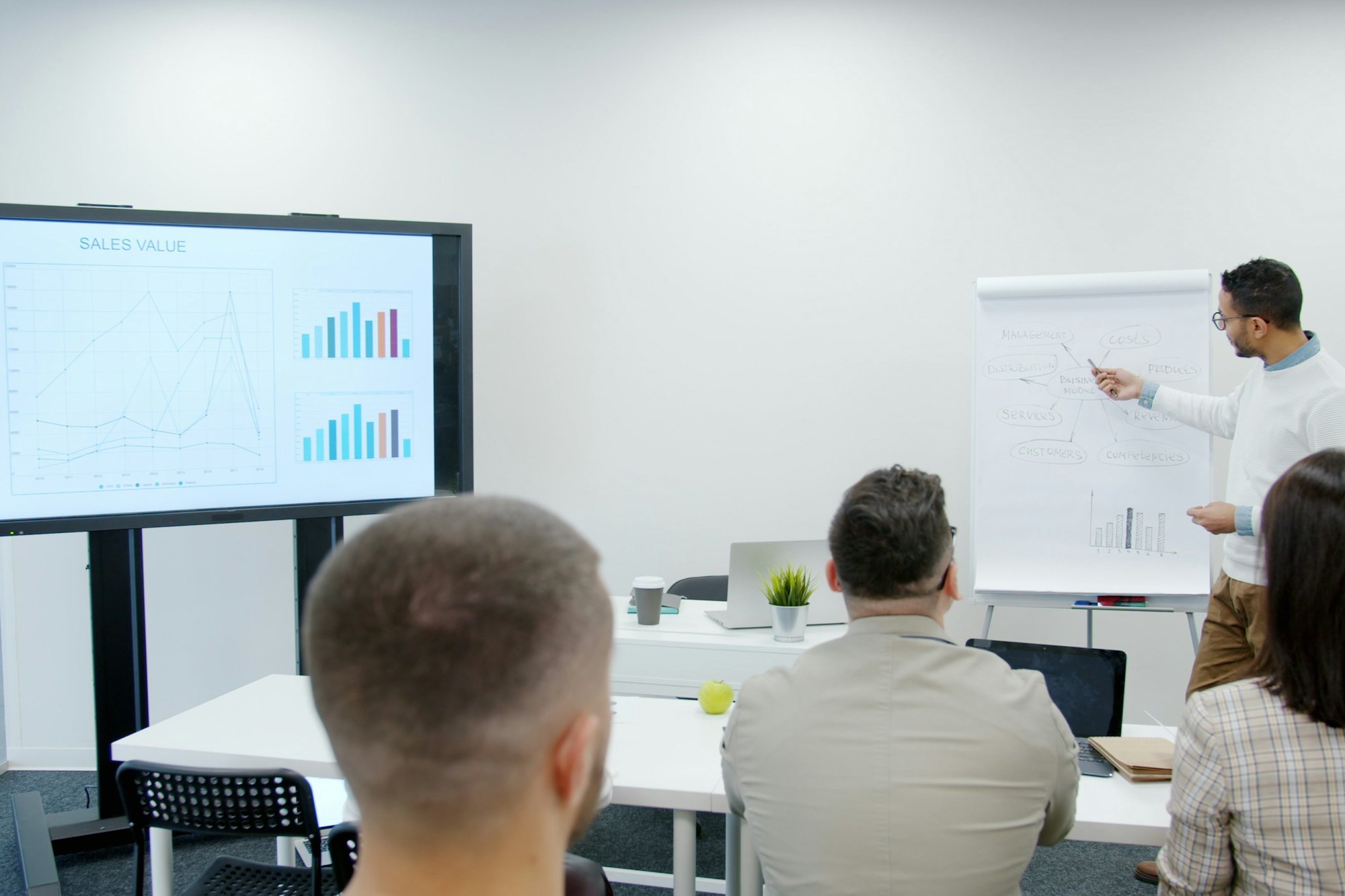 A training session in a bright room: a presentation screen and a flip chart at the front, people following from their seats