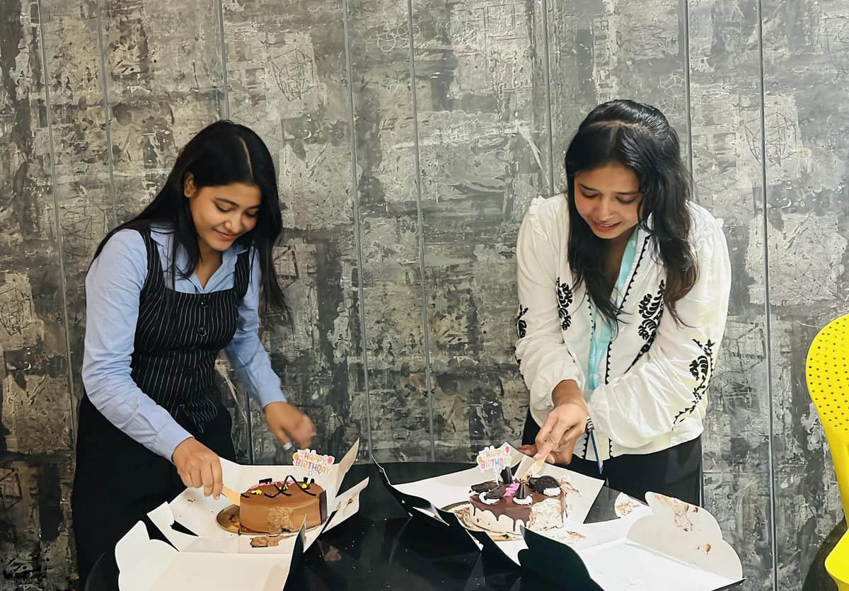 Two colleagues cutting birthday cakes in the office